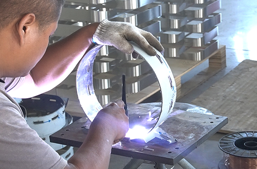 TIG welding a metal ring on a fixture, with sparks and a wire spool nearby